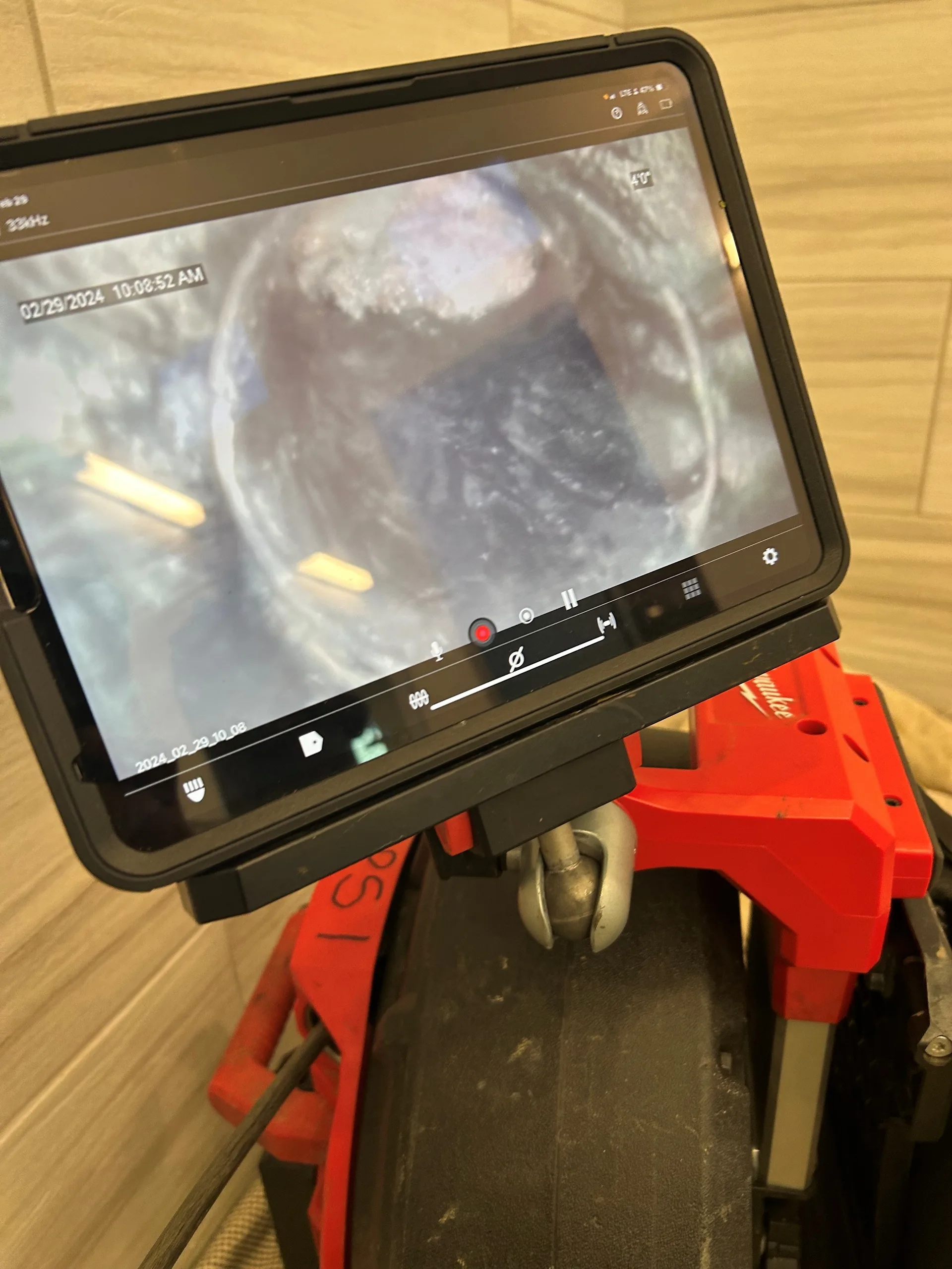 Tablet monitor on a sewer camera reel showing live video from inside a drain line