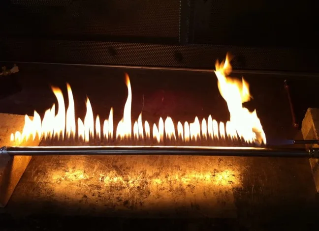 Lit gas log lighter pipe with a row of flames inside a fireplace