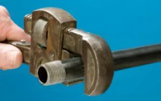 Hand holding a pipe wrench gripping a threaded black iron gas pipe