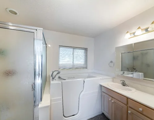 Bathroom with a white walk-in bathtub beside a glass-door shower and wood vanity