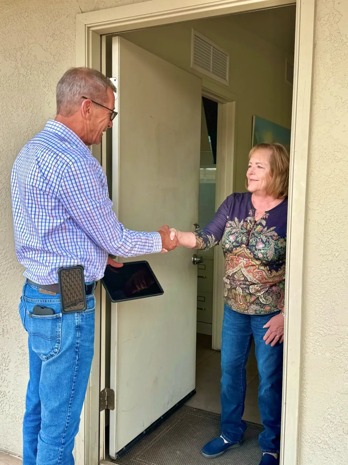 Tucson Plumbing representative with a tablet shaking hands with a homeowner at her front door