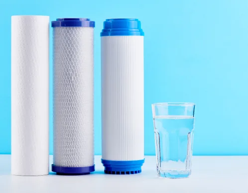 Three whole-home water filter cartridges lined up next to a glass of clean drinking water